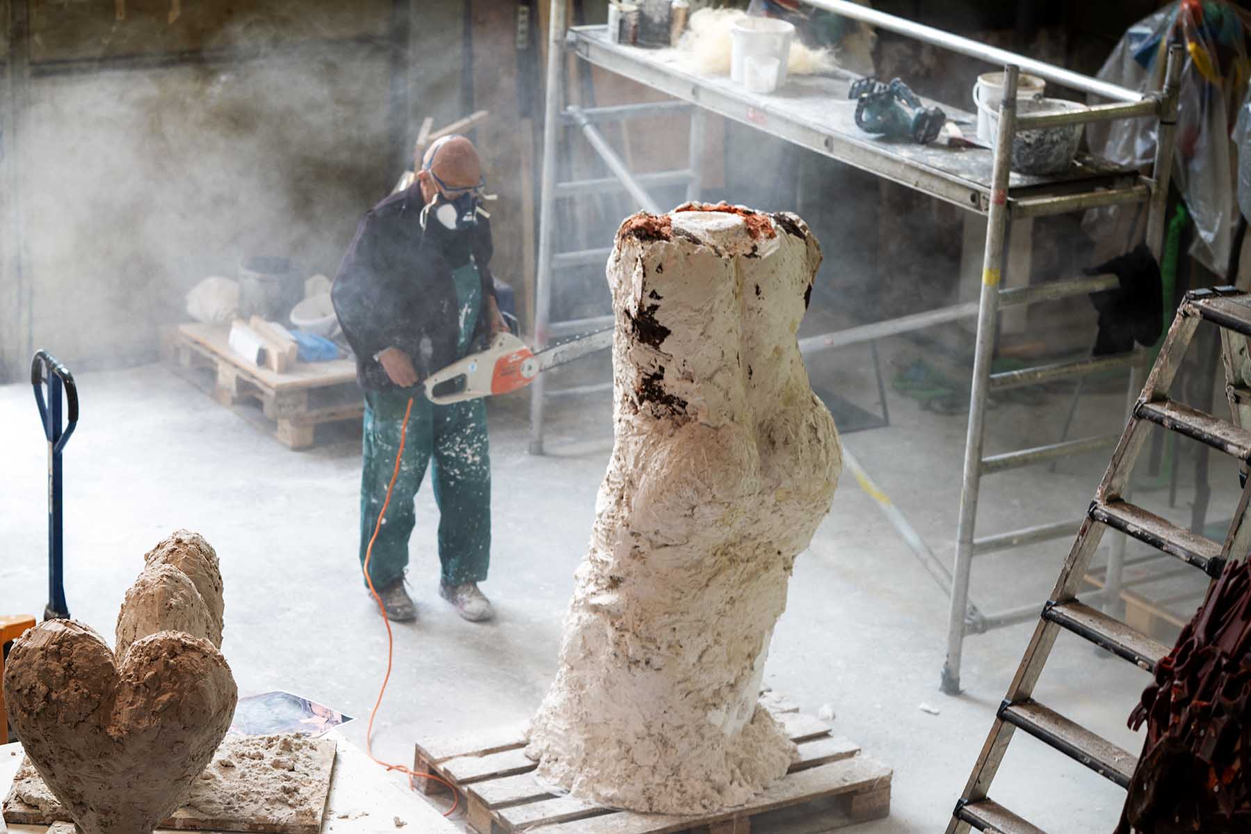 Jim Dine holds a chainsaw and works on a sculpture in his dusty Paris studio